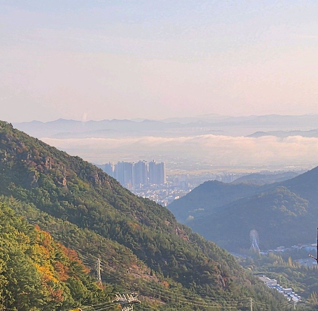 산비탈 아래 골짜기와 멀리 높은 아파트 단지, 그 뒤로 낮게 깔린 구름
